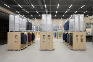 男裝精品零售空間，以結構鋼材展示架陳列西裝與襯衫，並搭配木質地板及玻璃隔間