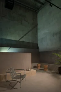 A minimalist lounge area with concrete walls and stools, featuring a striped armchair and a potted plant.