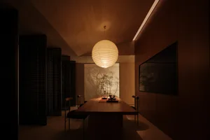 A modern dining room with a wooden table, chairs, and a round light fixture hanging from the ceiling. The walls are adorned w