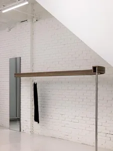 A modern clothing rack featuring a steel frame and oak wood accents, placed against a white brick wall in a minimalist interi