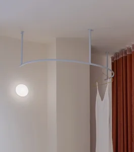 A modern metal clothing rack mounted on the ceiling with a light fixture and a white dress hanging on it.