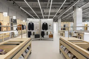 A modern retail interior shop that specializes in suits, featuring steel racks, glass panels, concrete flooring, and wooden s