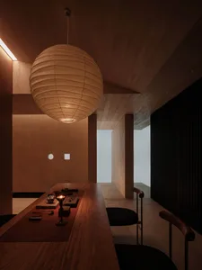 A minimalist tea room with wooden walls and floor, featuring a wooden counter and seating area, illuminated by a spherical pe