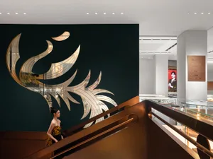 A woman in a yellow dress walking down a staircase with a metallic glazing wall and a gold-leafed phoenix artwork in a commer