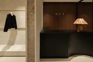 A minimalist shop interior featuring a black counter with a wood lamp, a black leather jacket hanging on a rod, and a marble 