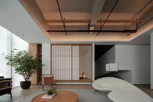 A minimalist living room featuring simple white furniture, a plant, and a round coffee table with a book and small plant.