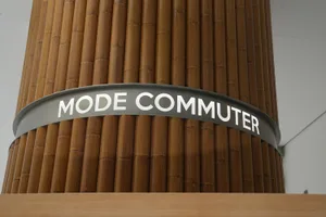 A branded column with the text 'MODE COMMUTER' on a metallic surface surrounded by wooden panels.