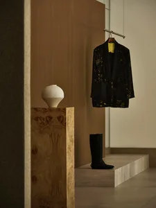 A minimalist clothing store with a wooden interior featuring a vase, coat, and boots.
