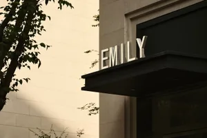 A large, modern building entrance sign made of metal with the name "EMILY" in capital letters.