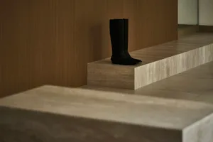 Modern minimalist shoe display made of concrete, featuring sleek black boots on a raised platform.