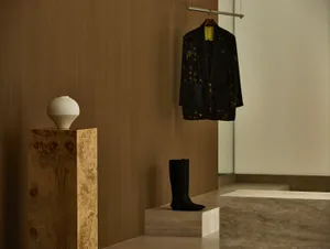 A minimalistic interior space featuring a stylish black jacket and a white vase on wooden pedestals.