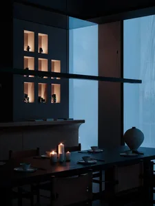 Modern minimalist dining table with glass top and wooden legs surrounded by chairs, featuring a wall display of illuminated v