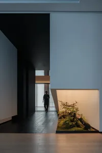 Man walking in a modern office space with black painted walls, OSB panel flooring, and a wooden desk in the foreground.