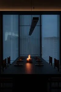 An elegant dining room with a long table set for dinner, featuring wood elements and soft candlelight.