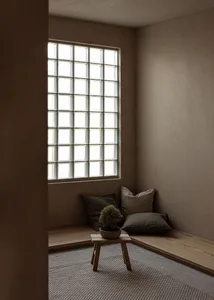 A cozy indoor space featuring wooden and concrete surfaces, with a small potted plant and cushions against the wall.