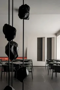 Industrial themed cafe interior featuring concrete floors and walls, with a large hanging rock art installation