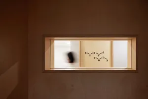 A rectangular window inset into a wooden wall, with a mural of interconnected letters inside.
