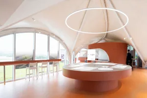 A clean, modern office space with concrete walls, a large table, and a circular light fixture.