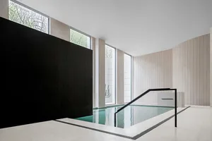 Modern swimming pool with concrete walls and floor, featuring tall windows and a black divider.