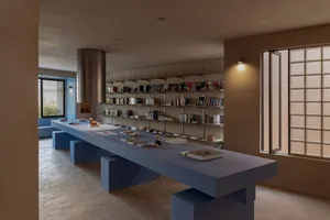 A spacious, industrial-style library with a concrete floor and walls, featuring a long table with books and a bookshelf fille