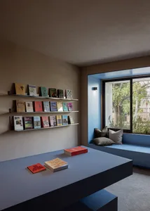 A minimalist library room with concrete walls, floating shelves, and a built-in bench seat.