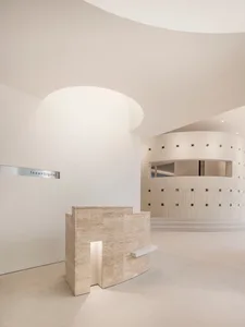 An Image of a minimalist office space with a reception desk made of concrete in a circular room with white walls and ceiling.