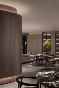 Modern dining room with wooden walls and chairs, marble table, and greenery centerpiece.