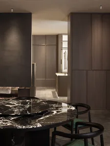 A modern kitchen with a round marble countertop and black chairs surrounded by dark wood cabinets.