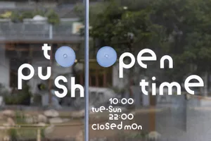 A glass storefront window with instructions to push to open, operating times, and days of closure.