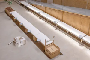 A spacious, industrial-style public area with long benches made of wood and covered in fabric.