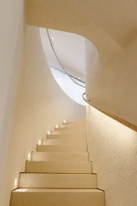 A modern staircase with concrete steps and walls, illuminated with small lights on the risers.