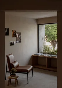 A modern living room with concrete walls and wooden accents, featuring a cozy corner seat and a window with greenery outside.