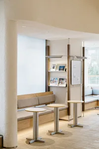 A modern reception area with wooden tables, a wooden bench, and metal shelving.