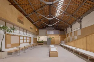 A spacious office interior with a high wooden ceiling, concrete flooring, and white seating areas.