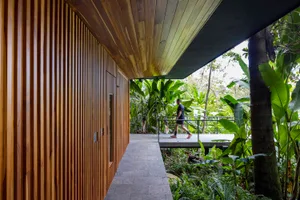 A modern architectural space featuring wooden walls and ceiling, surrounded by lush greenery.