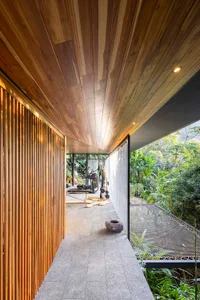 Indoor gym with wooden slats and concrete floor, featuring modern fitness equipment and lush greenery outside.