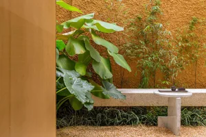 A modern landscape design featuring a concrete patio with gravel flooring and lush greenery.