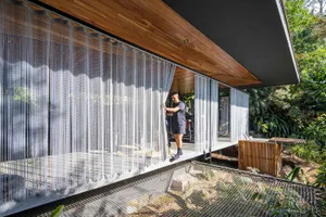 A modern residential interior featuring glass walls and chain curtains on a balcony.