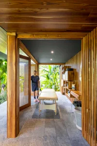 A person walking into a wooden spa treatment room with a massage table and shelves.