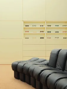 A modern, minimalist sunglasses shop featuring black leather seating and yellow painted walls.