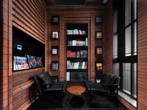 A cozy industrial-style lounge featuring a corner setup with black chairs and a wooden table, surrounded by brick walls and s