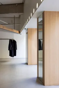 A modern clothing store with concrete walls, glass partitions, and wooden accents.