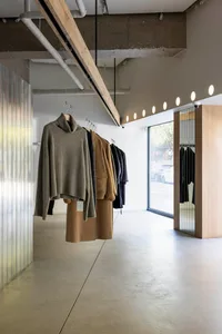 Modern retail store with clothing on racks, concrete floor, wooden walls and ceiling beams, glass window on the right, and ce