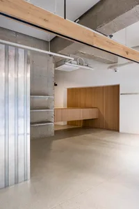 A modern office space with concrete flooring, minimalist wooden furniture, and industrial elements.