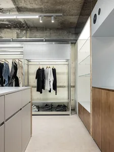 極簡服裝零售店，混凝土牆面搭配白色層架，展示各式服裝單品。