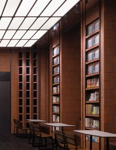 A modern library interior with high ceilings, tall brick walls, and wooden flooring. Features include tall bookshelves filled