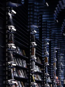 A modern library with metal shelves containing various books and illuminated by evenly spaced lights.