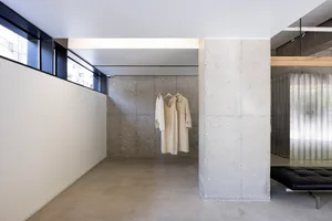 Creme-colored minimalist clothing items displayed on a concrete wall within a minimalist interior space.