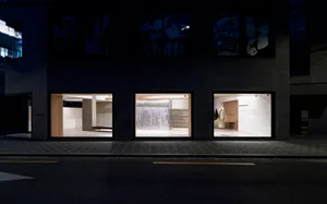 A modern retail storefront illuminated from within at night, showcasing minimalist design elements and metal window displays.