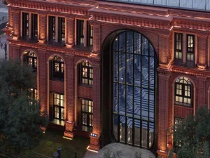 The exterior of a brick building illuminated at night, featuring arched windows and a large glass entrance.